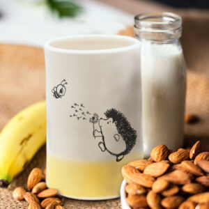 Handmade ceramic tumbler with drawing of a hedgehog blowing on a dandelion for a bee to enjoy. Gold accent color