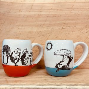 Two handmade cocoa mugs with drawings of hedgehogs doing ridiculous things like YMCA karaoke and sunbathing